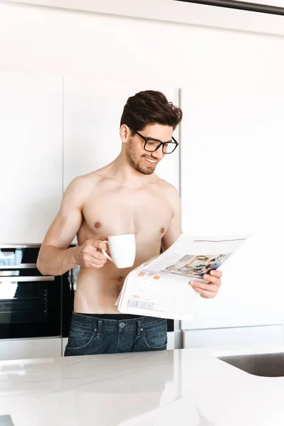 Imagen Joven Sonriente Parado Cocina Leyendo Periódico Tomando Café Mirando — Foto de Stock