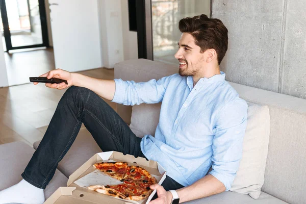 Smiling Young Man Holding Remote While Sitting Couch Home Eating — Stock Photo, Image