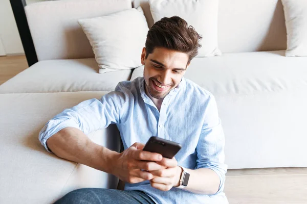 Joven Sonriente Usando Teléfono Móvil Mientras Está Sentado Sofá Piso — Foto de Stock