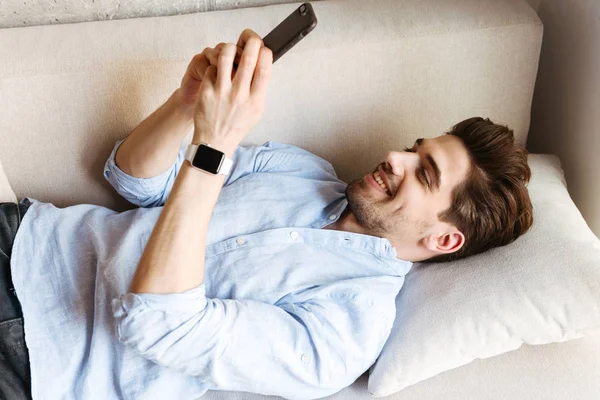 Sonriente Joven Usando Teléfono Móvil Mientras Está Acostado Sofá Casa — Foto de Stock