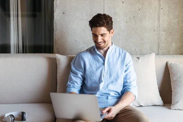 Retrato Jovem Sorridente Usando Computador Portátil Enquanto Sentado Sofá Casa — Fotografia de Stock