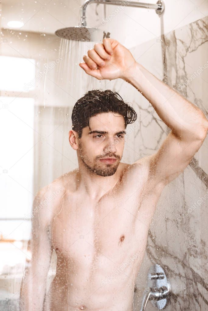 Charming young naked man having a shower