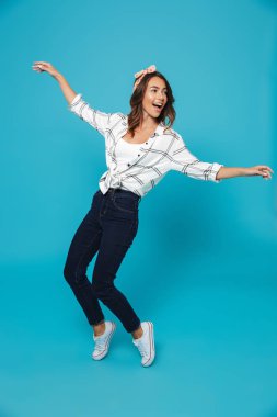 Tam uzunlukta portresi atlama bir neşeli genç ev hanımı, seyir uzağa mavi arka plan üzerinde izole