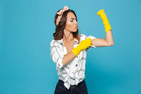 青い背景に分離を清掃中の手の保護のための黄色のゴム製手袋を着用しながら素敵な強い主婦 代表示力こぶの肖像画 — ストック写真