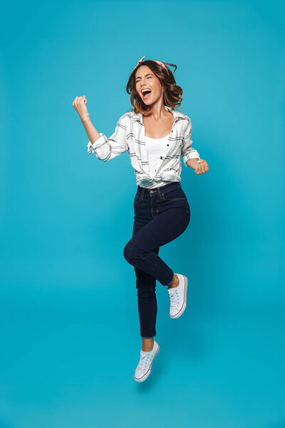 Full length portrait of a happy young housewife jumping isolated over blue background