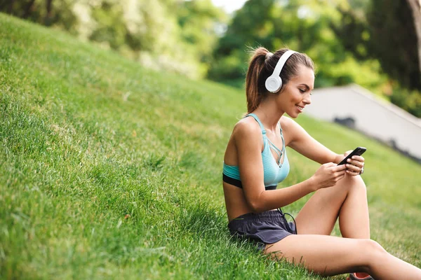 Satisfied Young Sportswoman Dressed Sportswear Headphones Resting While Sitting Grass — Stock Photo, Image