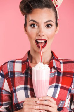 Heyecanlı sürpriz genç pin-up kadın kokteyl elinde pembe bir arka plan duvar üzerinde izole görüntüsünü.