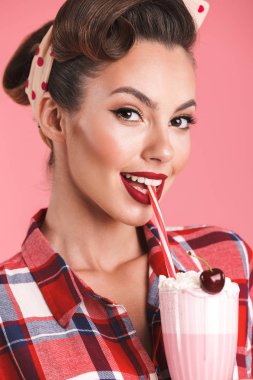 Neşeli esmer pin-up kızı ekose gömlek içme süt sallamayın portresi kadar pembe arka plan üzerinde kapatın