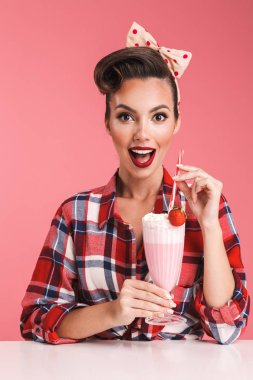 Heyecanlı sürpriz genç pin-up kadın kokteyl elinde pembe bir arka plan duvar üzerinde izole görüntüsünü.