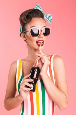 Soda şişesi ile ayakta ve uzak pembe arka plan üzerinde seyir mayo gülümseyen bir esmer pin-up kızı portresi