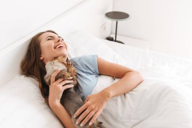 Evde yatakta döşeme iken süre köpekle oynamayı mutlu genç kadın