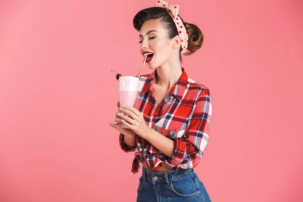 一个开朗的黑发女孩的肖像在格子衬衫喝牛奶动摇粉红色背景 — 图库照片
