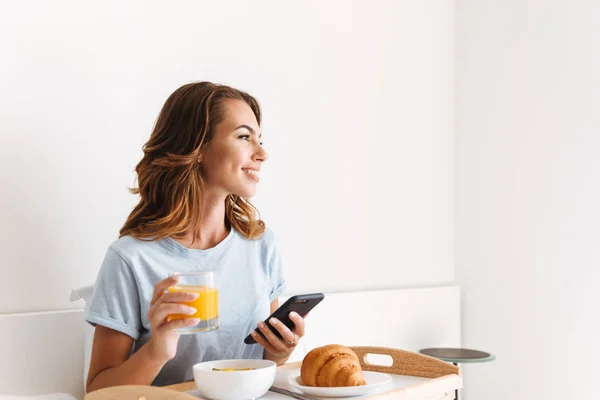 Mujer Joven Sonriente Sosteniendo Teléfono Móvil Mientras Desayuna Una Bandeja —  Fotos de Stock