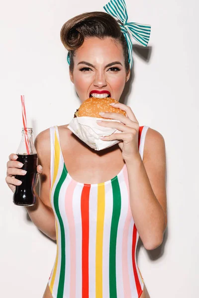 Образ красивий підколоти жінка ізольовані над білі стіни фон їжі burger питної соди. Дивлячись камера. Ліцензійні Стокові Фото