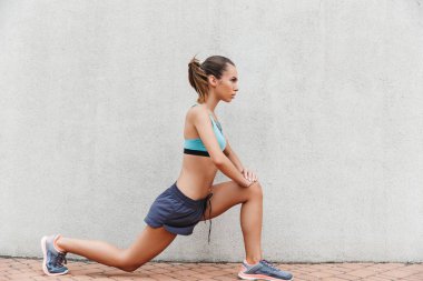 Kendine güvenen genç sporcumuz yan görünüm açık havada duvara germe egzersizleri yapıyor spor giyim giyinmiş