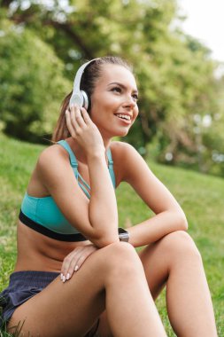 Heyecanlı genç sporcumuz açık havada çimenlerin üzerinde otururken dinlenme kulaklık spor giyim giymiş