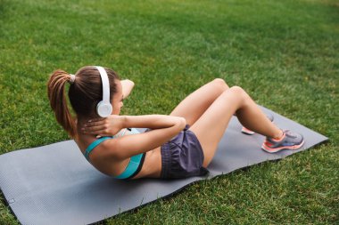 Spor fitness mat açık havada çimenlerin üzerinde ısınma sırasında kulaklık ile müzik dinlemek genç sporcumuz yan görünüm giymiş