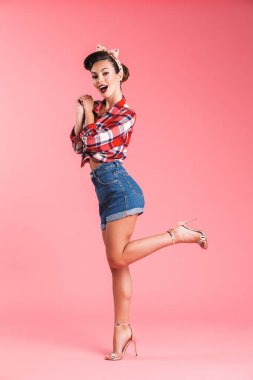 Heyecanlı bir esmer pin-up kızı ekose gömlek pembe arka plan üzerinde poz kameraya bakarak tam uzunlukta portresi