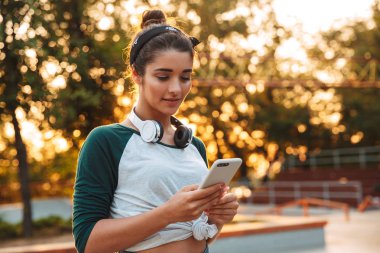 Cep telefonuyla dururken parkta kulaklık ile neşeli genç kız