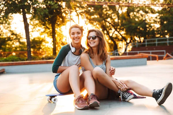 Dos Chicas Jóvenes Sonrientes Divirtiéndose Mientras Están Sentadas Con Monopatín —  Fotos de Stock