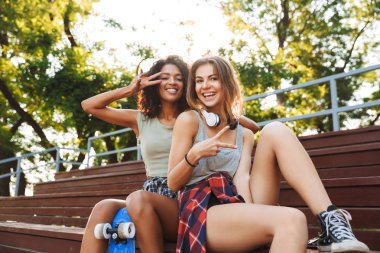 İki genç kız ile birlikte parkta otururken eğleniyor kaykay heyecan