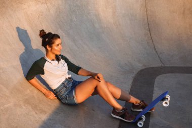 Genç kız rampa oturan kaykay ve kulaklık ile gülümseyen