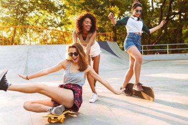 Üç genç kız parkta birlikte eğleniyor kaykaylar ile gülüyor