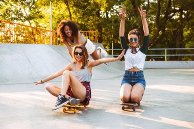 Üç genç kızlar ile birlikte parkta eğleniyor kaykaylar heyecanlı