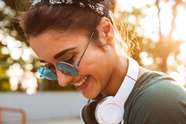 Güneş gözlüğü ve kulaklıklar açık havada giyen bir gülümseyen genç kız yakın çekim