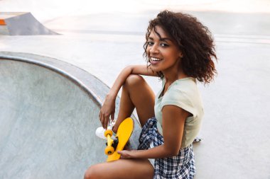 Neşeli genç afro amerikan kız kaykay ile bir parkta oturan