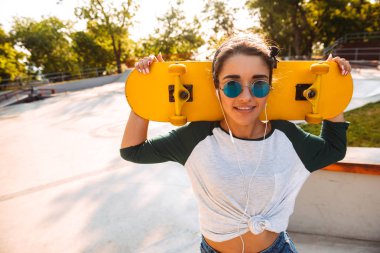 Açık havada kaykay kulaklık ile müzik dinleme ile yürüyen genç mutlu neşeli kadın fotoğrafı.