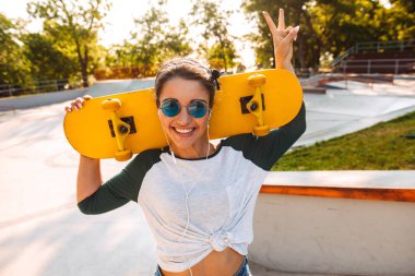 Barış gösterilen kaykay ile açık havada yürüyen genç mutlu neşeli kadın fotoğrafı jest kulaklık ile müzik dinleme.