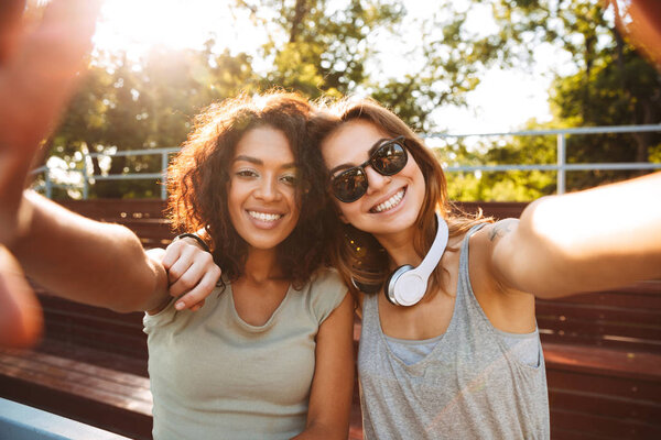 Two excited young girls having fun while taking selfie together at the park