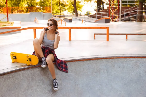 Jovencita Alegre Auriculares Escuchando Música Mientras Está Sentada Con Monopatín — Foto de Stock