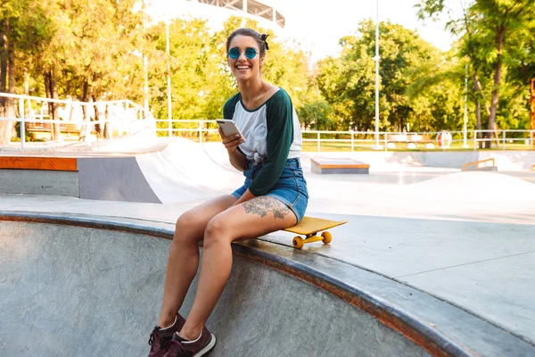 Photo Young Happy Cheerful Woman Sitting Outdoors Skateboard Using Mobile — Stock Photo, Image
