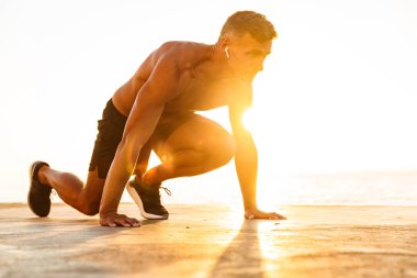 Plajda güneş ışığı altında yayınlanmaya başlaması hazır Başlarken kulaklık ile kendine güvenen sporcu