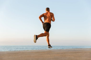 Gömleksiz sporcu plajda çalışan kulaklıklar ile arkadan görünüm
