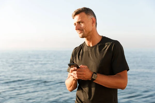 Smiling Sportsman Using Mobile Phone While Standing Beach — Stock Photo, Image