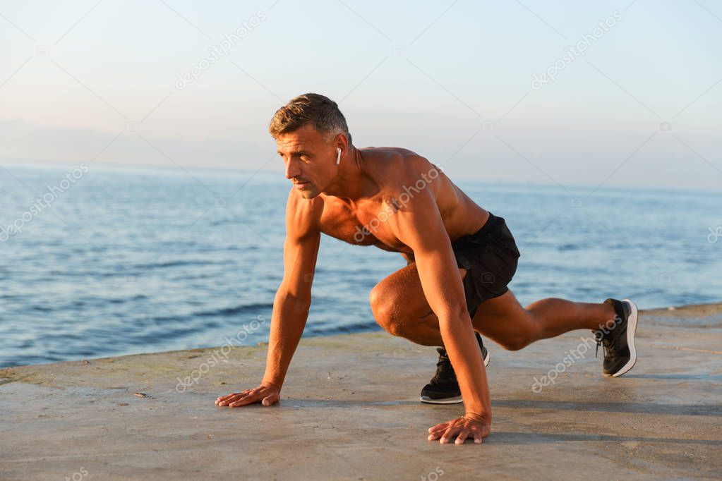 Concentrated sportsman with earphones getting ready to start running at the beach