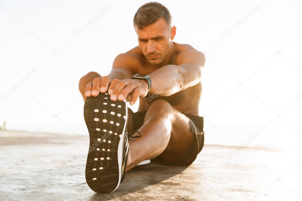 Confident shirtless sportsman doing stretching exercises at the beach