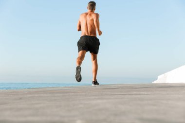 Sahilde açık havada çalışan güçlü olgun sporcunun görünüm görüntüsü geri.