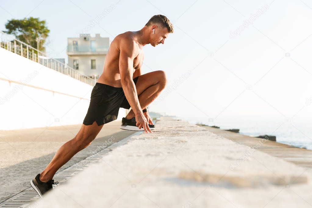 Image of handsome strong mature sportsman make sport exercises on the beach outdoors.