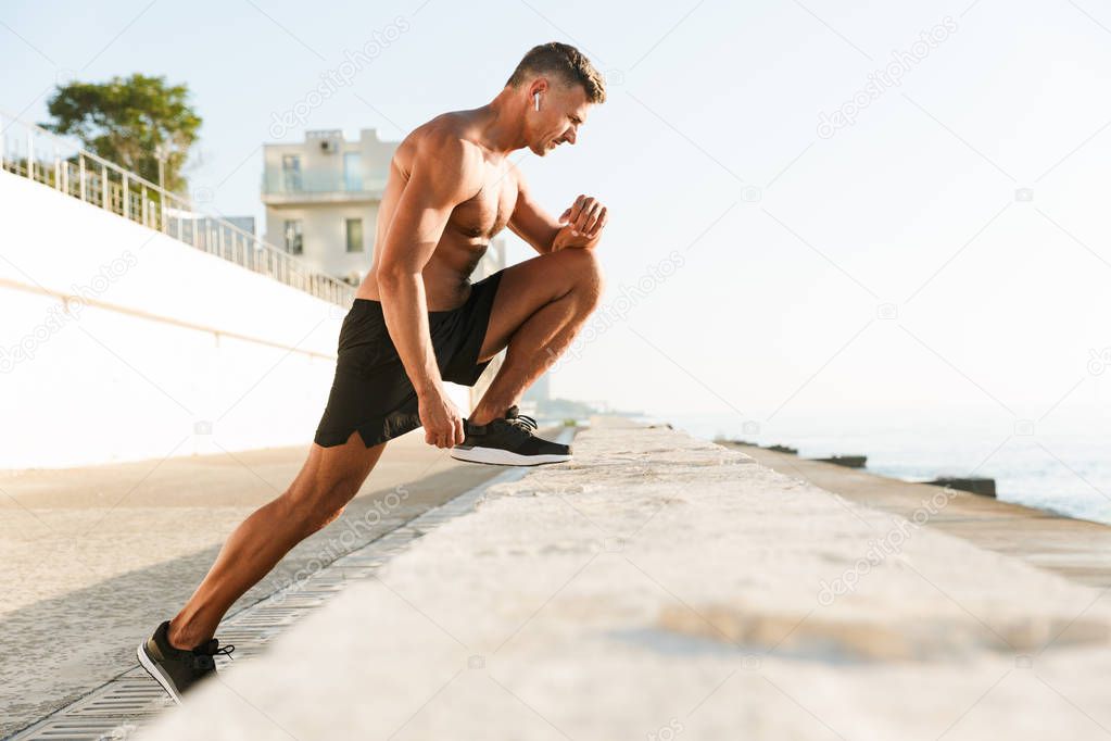 Image of handsome strong mature sportsman make sport exercises on the beach outdoors.