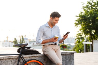 Gülümseyen genç şık adam açık havada bisiklet ile kahve yudumlarken istimal hareket eden telefon
