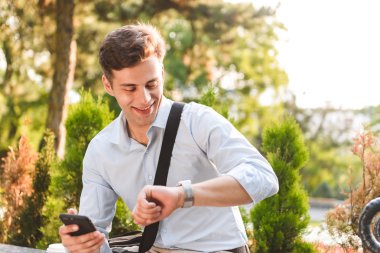 Onun cep telefonu açık havada tutarak bakarak gömlek gülümseyen genç bir adam portresi giymiş