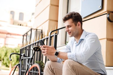 Şık delikanlı büyüleyici bir şehir sokak, bir bisiklet ile oturma ve cep telefonuyla gömlek giymiş