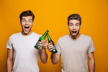 Sarı arka plan üzerinde izole bira şişeleri ile kızartma bir neşeli genç erkekler en iyi iki arkadaş portresi