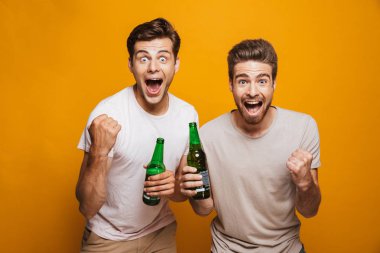İki mutlu genç adam portresi en sarı arka plan üzerinde izole kutlama bira şişeleri ile toasting yakın arkadaşlarım