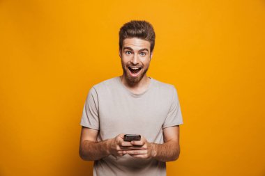 Cep telefonu sarı arka plan izole tutan mutlu bir genç adam portresi