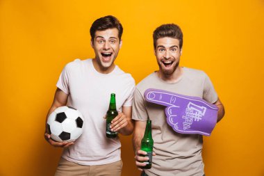Bira şişesi holding ve sarı arka plan üzerinde izole bağırarak futbol topu ile iki mutlu genç adam portresi en yakın arkadaşlarım